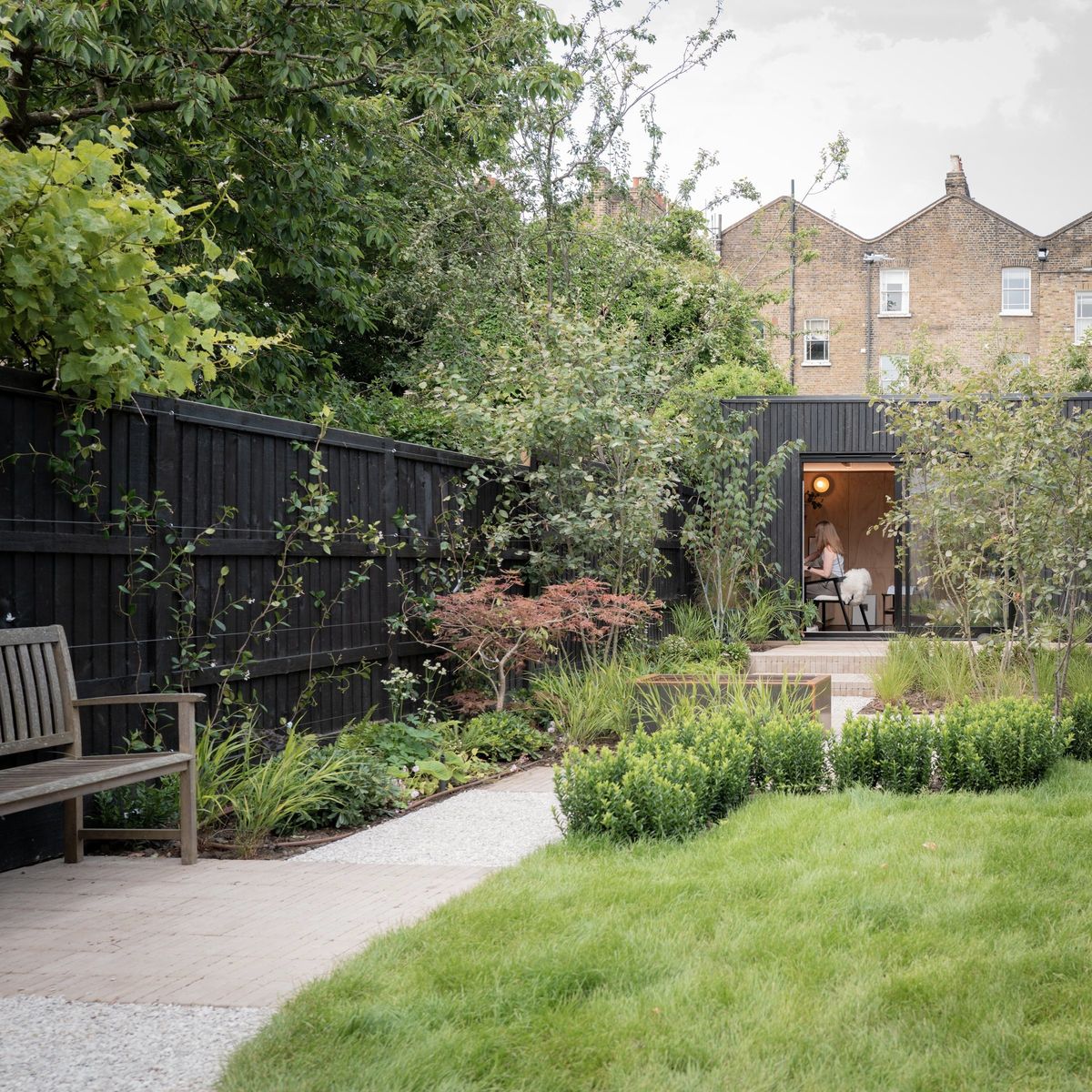Path through a planted garden in Peckham to a charred-timber garden studio at the far end