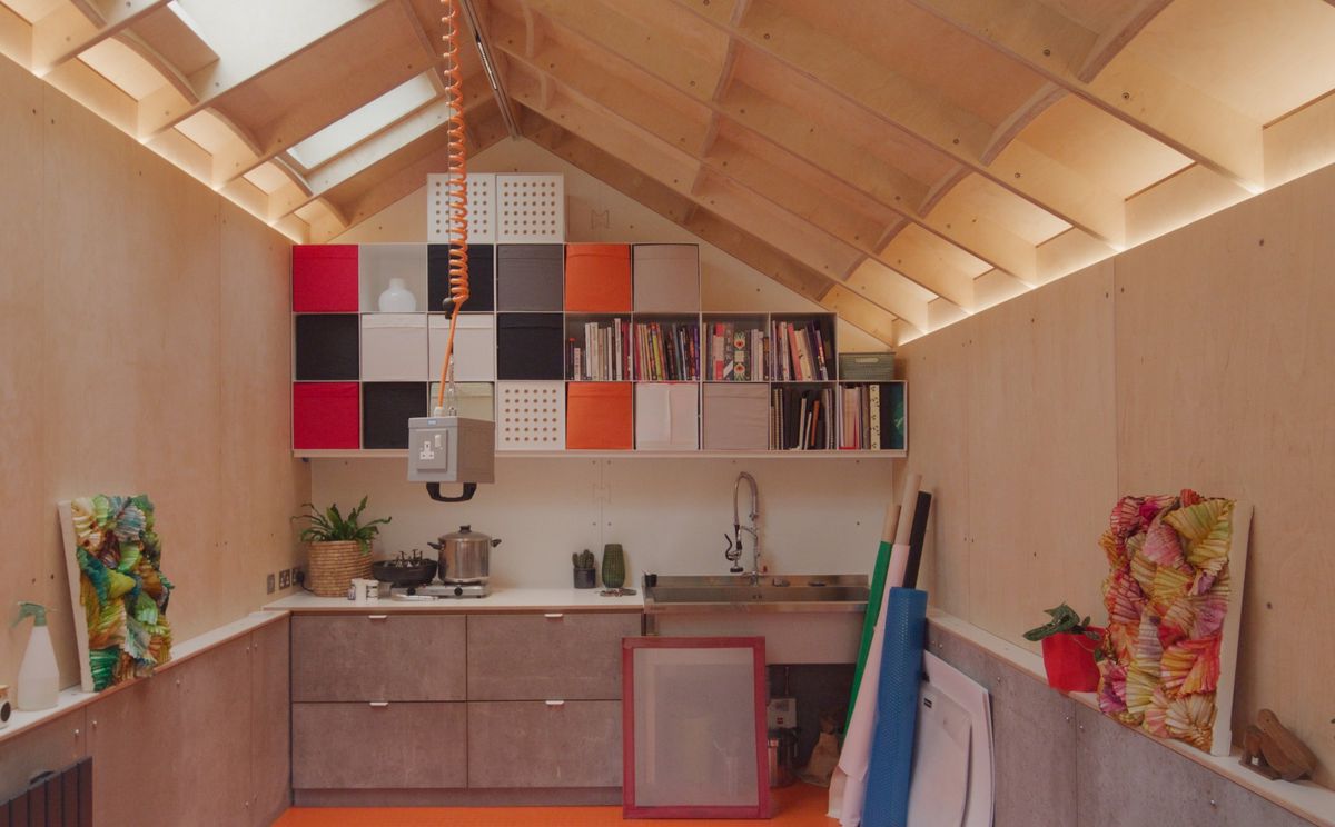 Inside a pitched-roof garden room used as an artist’s studio in Haringey: birch rafters, skylights and colourful storage