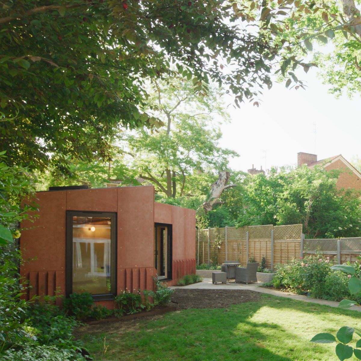 Red V-shaped garden room at the end of a lawn in a Canonbury conservation area, framed by trees